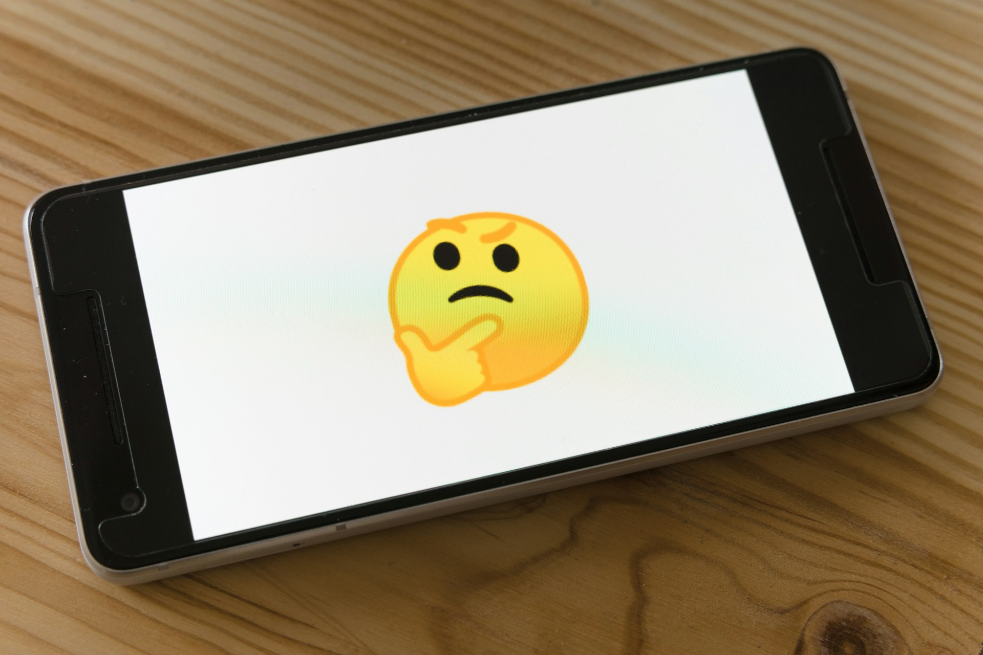 An image of a mobile phone with the 'thinking face' emoji on the screen.  Photo by Markus Winkler on Unsplash.